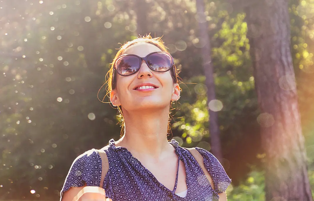 Woman waring sunglasses, looking up, and smiling